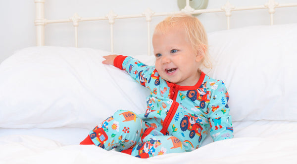 A smiling toddler wearing a colourful Ducky Zebra zip-up sleepsuit