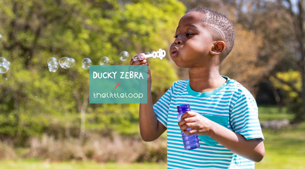 Image of a boy blowing bubbles wearing a turquoise stripe Ducky Zebra t-shirt with logos from Ducky Zebra and thelittleloop'