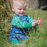 Smiling baby sitting in the grass, wearing a Ducky Zebra unisex baby outfit - including a green striped top and a blue patterned romper