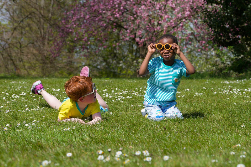 Image of two happy boys, sitting and lying in the grass, surrounded by daisies wearing Ducky Zebra clothes and challenging stereotypes, with one wearing pink trainers