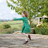 Image of girl running outside, wearing a Ducky Zebra green dress with a fun print of hedgehogs and dogs gardening