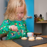 Image of girl cooking, wearing a green Ducky Zebra skater dress with a fun dog and hedgehog print.