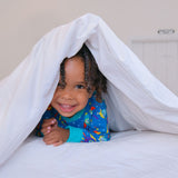 Fun photo of a child peeking out of a white duvet wearing Ducky Zebra space themed, unisex pyjamas.