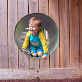 A boy peaking out of a tunnel wearing fun, colourful Ducky Zebra shorts and sweatshirt
