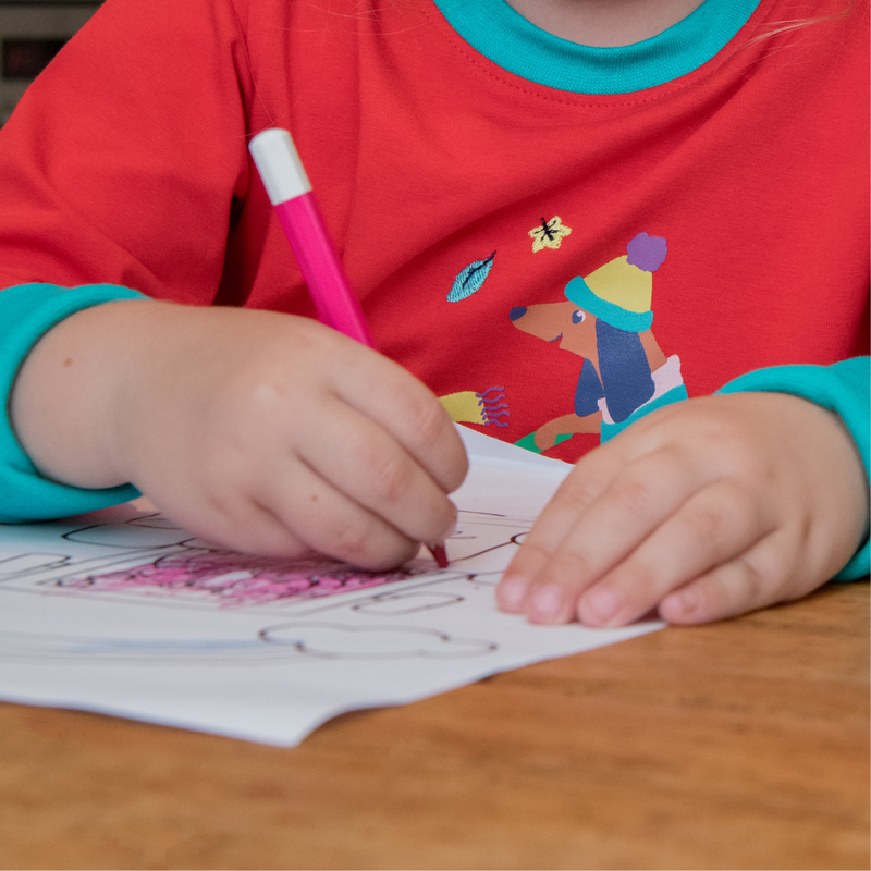 Close up of child colouring while wearing a red Ducky Zebra top with a sausage dog on it.