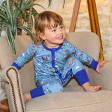 Smiling toddler wearing Ducky Zebra x Roald Dahl zip-up sleepsuit, with a fun print, featuring animals from Roald Dahl stories, including the newt from "Matilda," Alfie the tortoise from "Esio Trot," and Muggle-Wump the monkey from "The Twits".