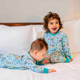 Toddler and baby sitting together on a bed, with the toddler wearing Ducky Zebra Roald Dahl PJs and the baby wearing a twinning organic cotton sleepsuit.