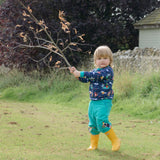 A boy outside wearing Ducky Zebra turquoise cords and a Ducky Zebra blue sweatshirt with a festival all over print. He's holding a branch and looking straight at he camera