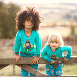 A girl and boy standing side by side on a gate, both wearing colourful Ducky Zebra clothes including a turquoise top with a rocket applique