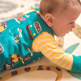 Baby lying on a patterned rug wearing a pair of Ducky Zebra teal dungarees with a yellow and white bodysuit below.