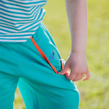 Image of a child wearing a pair of unisex turquoise shorts with the pocket pulled open. Inside the pocket we can see an embroidered splash motif