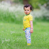 Boy wearing colourful unisex yellow t-shirt with Ducky Zebra joggers. He's standing in the grass, looking curiously at the camera.