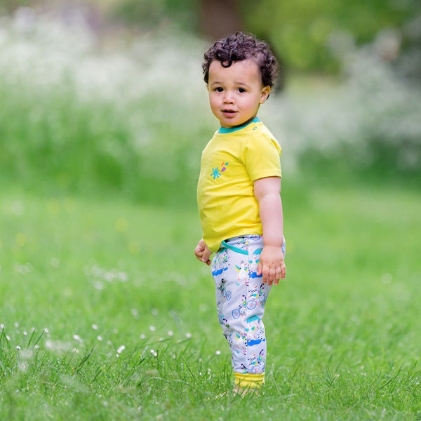 Boy wearing colourful unisex yellow t-shirt with Ducky Zebra joggers. He's standing in the grass, looking curiously at the camera.