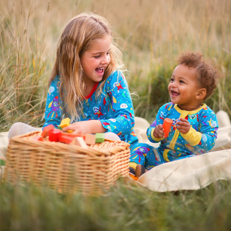 Image of a girl and baby sitting side by side in the long grass. They're wearing Ducky Zebra twinning organic cotton outfits, both with a colouful space theme.