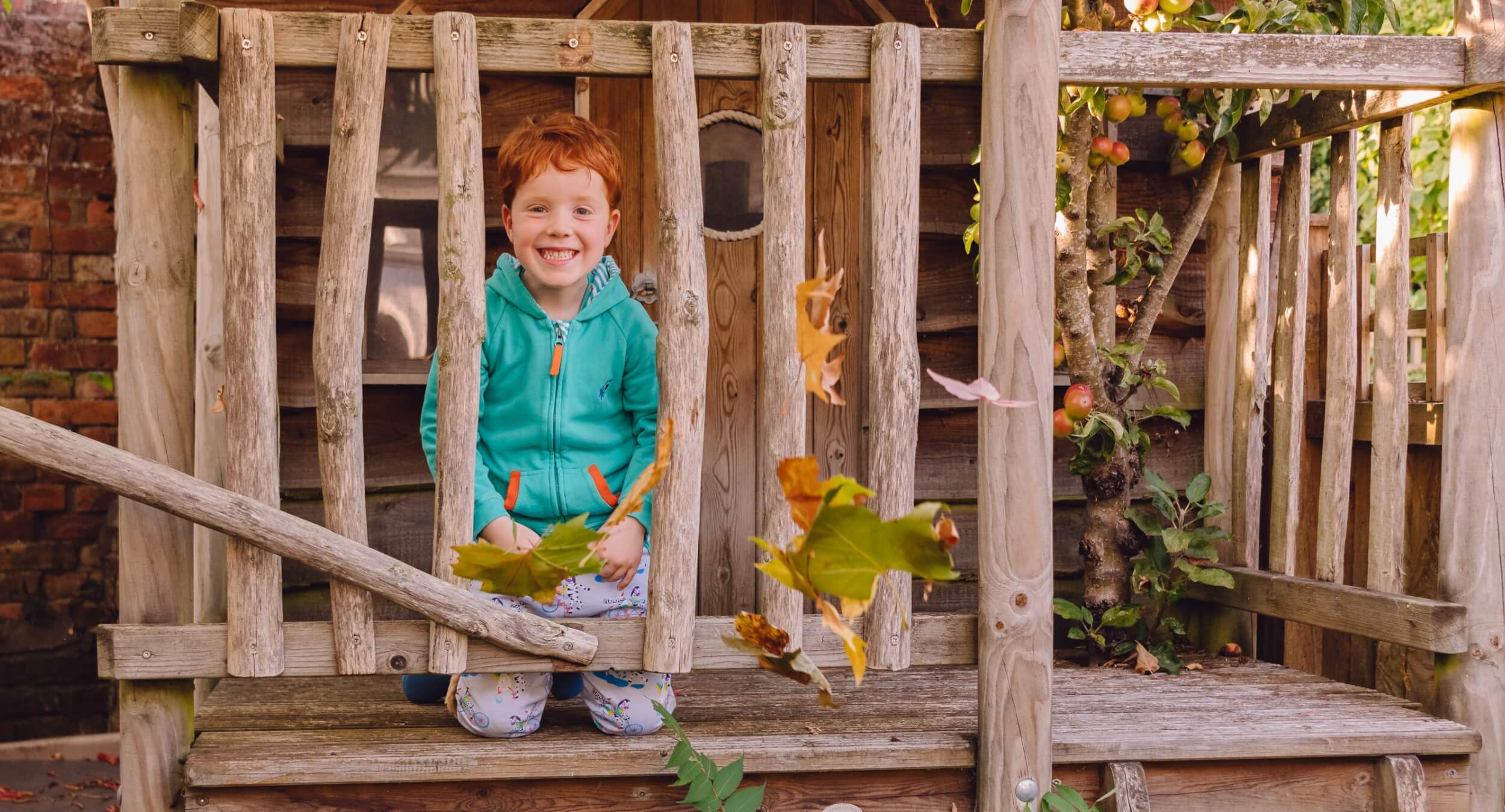Image of smiling boy in a tree house wearing Ducky Zebra organic cotton clothes