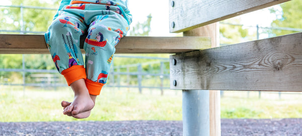 Image of a child's feet dangling below a bench wearing Ducky Zebra green Trousers with a Canoe Print