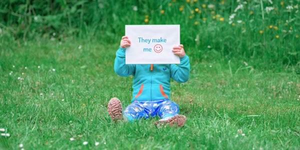Boy wearing colourful clothes holding a sign that says "They make me happy"