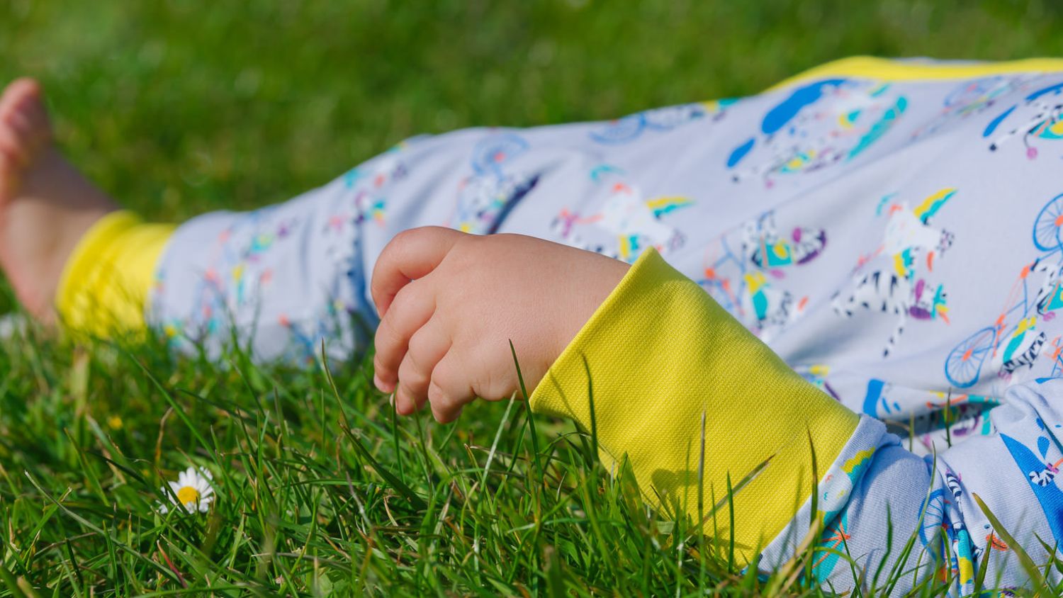 Toddler lying in the grass wearing a Ducky Zebra Zip Sleepsuit 