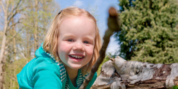 Image of a happy, smiling girl outside poking a stick into the lens of the camera. The girl is wearing a turquoise Ducky Zebra hoody.
