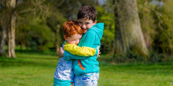 Two kind, happy boys outside hugging one another. The boys are wearing colourful Ducky Zebra clothes