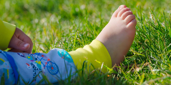 Image of a baby wearing a Ducky Zebra romper, with bare feet on the grass