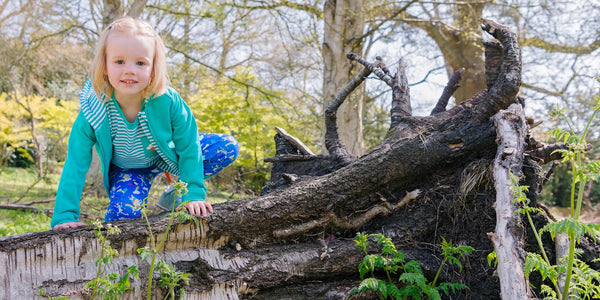 Image of a smiling girl climbing a fallen tree, wearing Ducky Zebra clothes