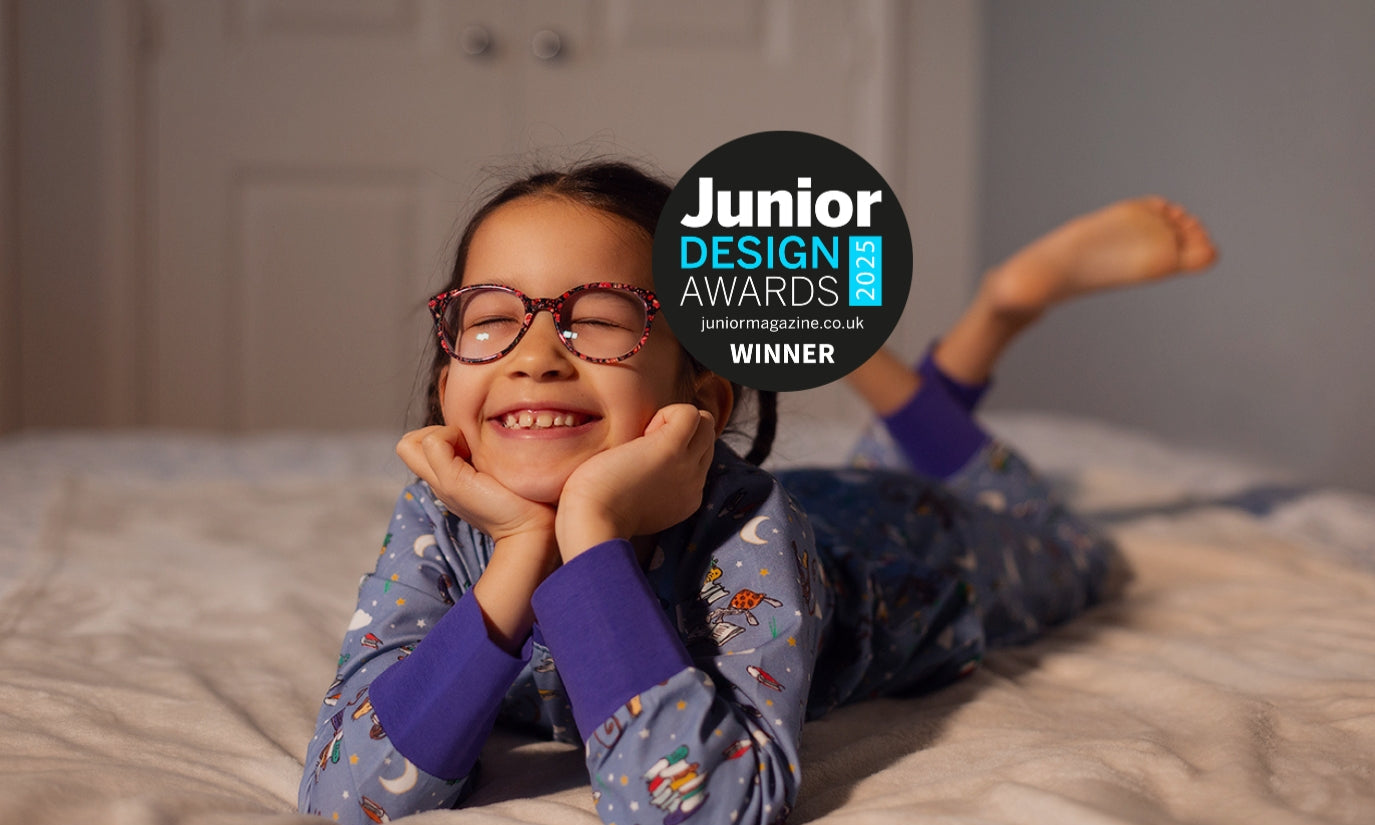 Smiling girl lying on the bed, wearing Ducky Zebra x Roald Dahl Pyjamas and a Junior Design Award 'Winner' badge on top