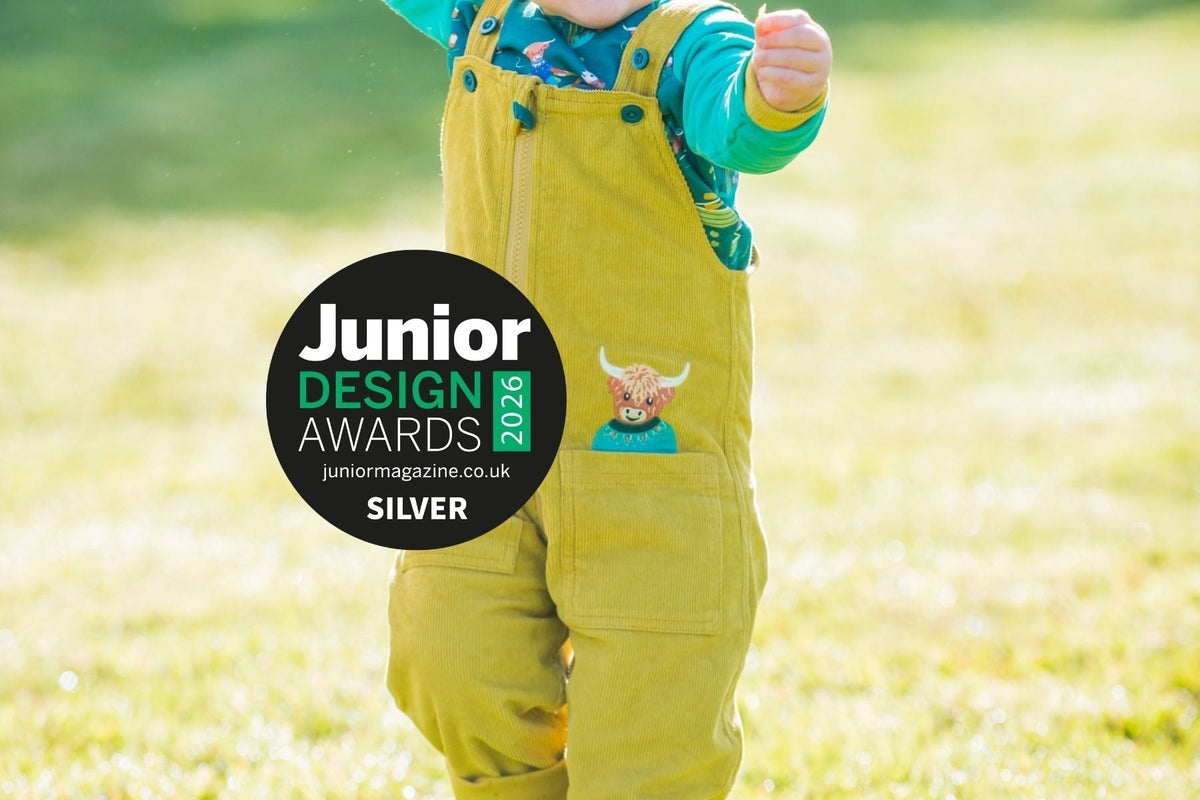 Image of child wearing yellow dungarees with a highland cow poking out of the pocket. The picture has the Junior Design Awards logo on top.