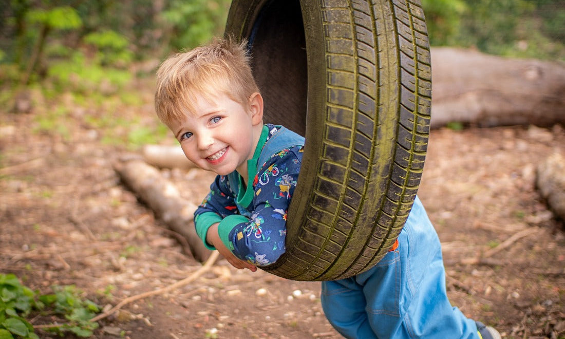 Boy lying on a tyre swing, wearing Ducky Zebra unisex dungarees and top