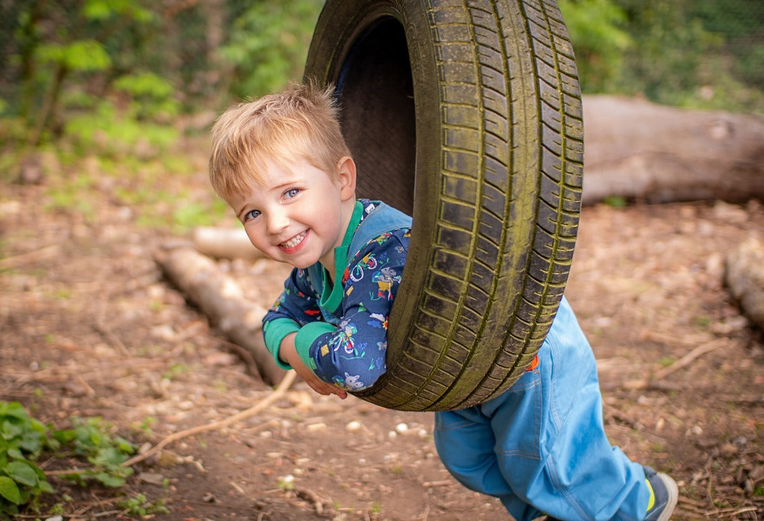 Boy lying on a tyre swing, wearing Ducky Zebra unisex dungarees and top