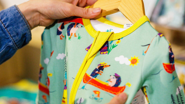 A close up of someone holding a baby Ducky Zebra sleepsuit on a hanger