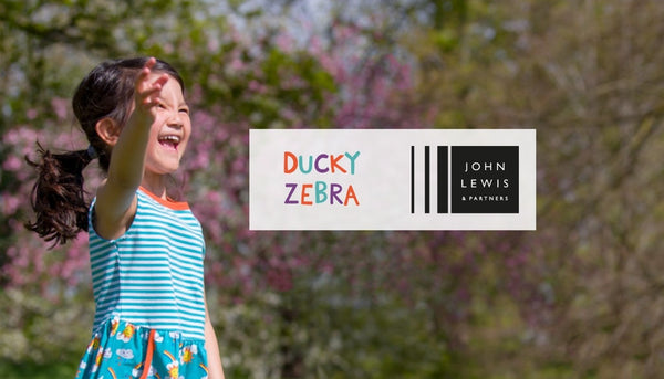 Image of a girl smiling and wearing a Ducky Zebra sleeveless dress with the John Lewis and Ducky Zebra logos by her side