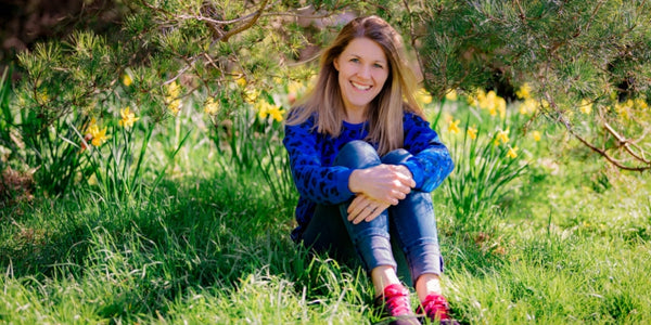 Image of Sally Dear, founder of Ducky Zebra, sitting in the grass with her arms wrapped around her legs