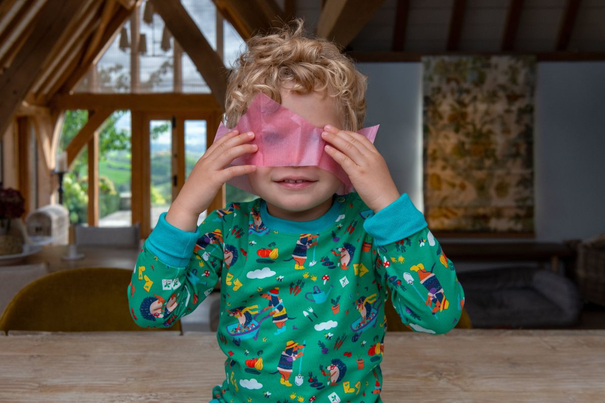 Smiling boy wearing a pink party hat and green Ducky Zebra unisex top