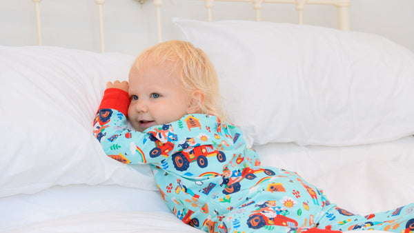 Baby lying on a bed, wearing a Ducky Zebra sleepsuit 