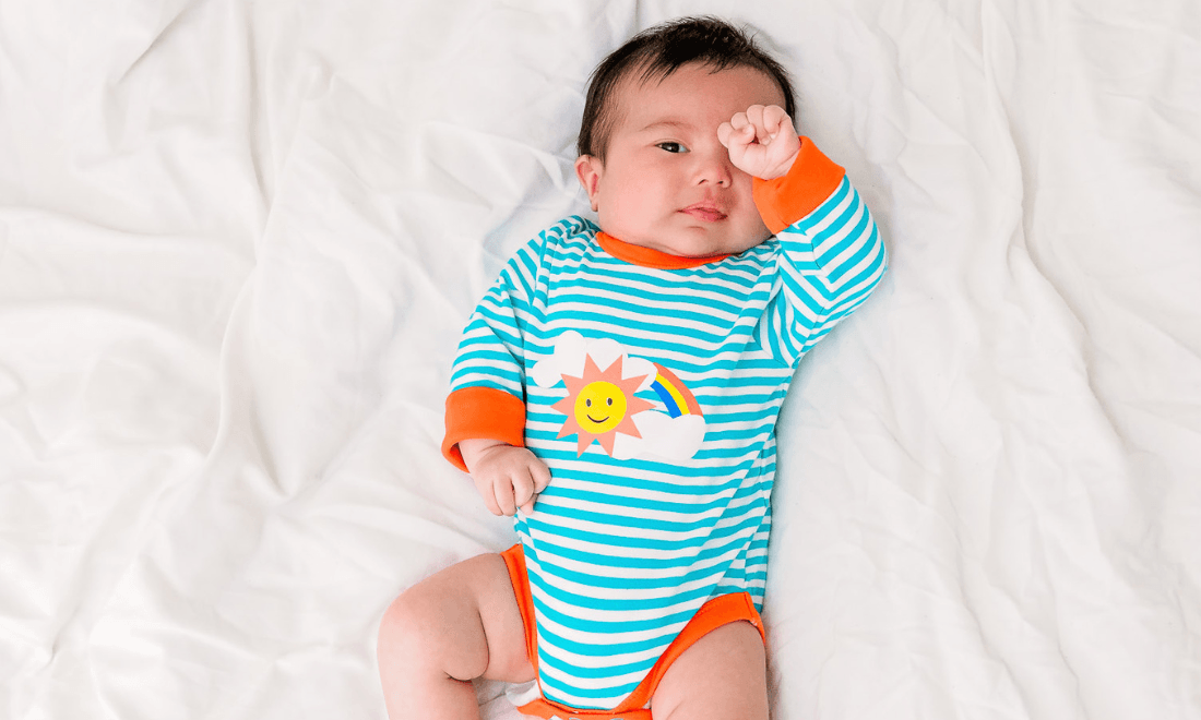 Baby wearing colouful unisex bodysuit with a rainbow print, by Ducky Zebra