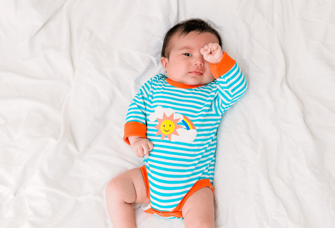 Baby wearing colouful unisex bodysuit with a rainbow print, by Ducky Zebra