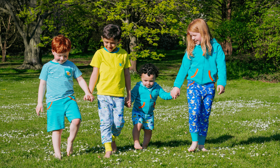 Children holding hands wearing unisex Ducky Zebra clothes, walking through the grass