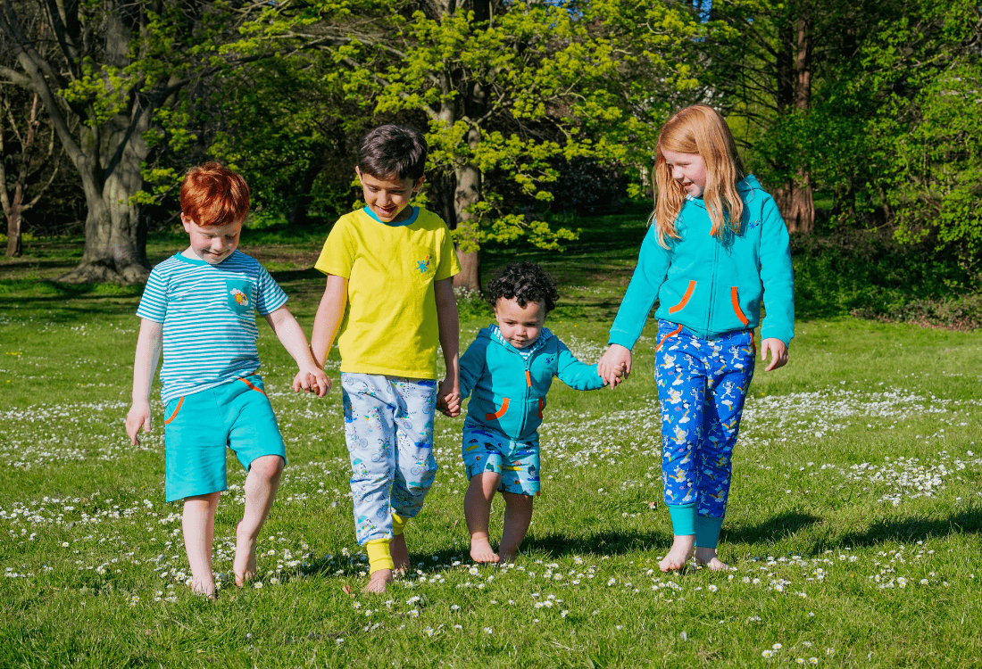 Children holding hands wearing unisex Ducky Zebra clothes, walking through the grass