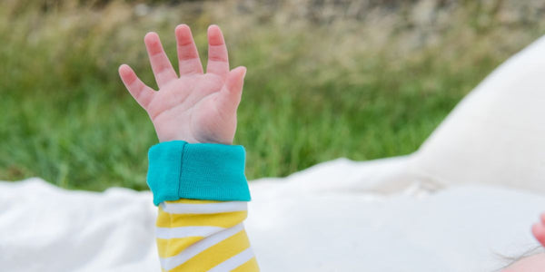 A baby's hand with 5 fingers held up, wearing unisex Ducky Zebra baby clothes