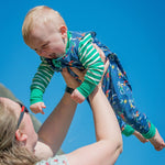Smiling baby being thrown into the air, wearing a Ducky Zebra unisex baby outfit, including a green stripe top and blue dungarees
