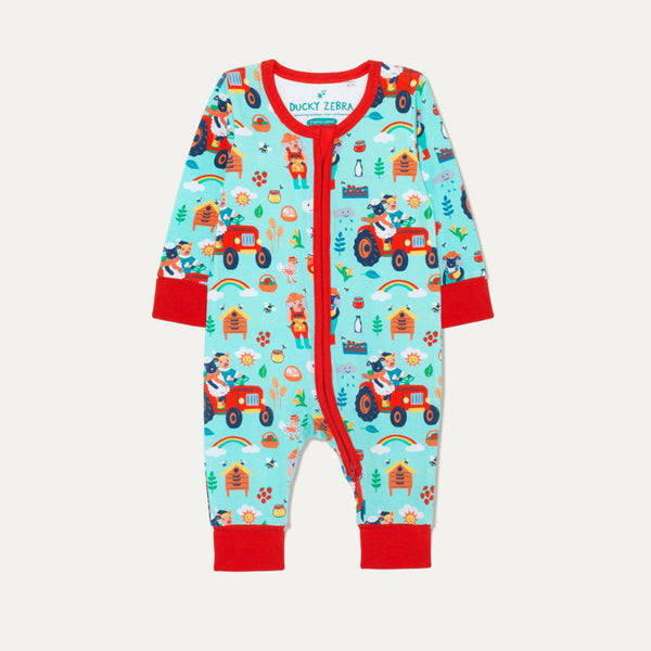 Unisex baby zip-up sleepsuit with a pale blue background and a fun repeat print of a sheep and pig driving their red tractor and looking after their bees. The sustainable romper has red contrasting cuffs, a two-way zip and chin guard. The cuffs are rolled-up in the picture.