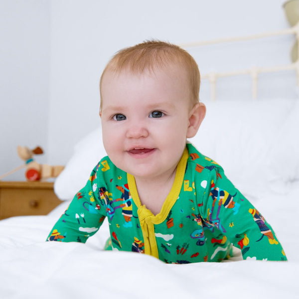 Image of baby smiling at the camera, wearing a green unisex sleepsuit with a yellow zip. 