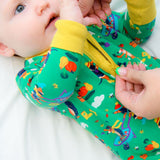 Image of a baby lying on a bed wearing a green Ducky Zebra sleepsuit. We can see a hand opening up the zip on the sleepsuit.