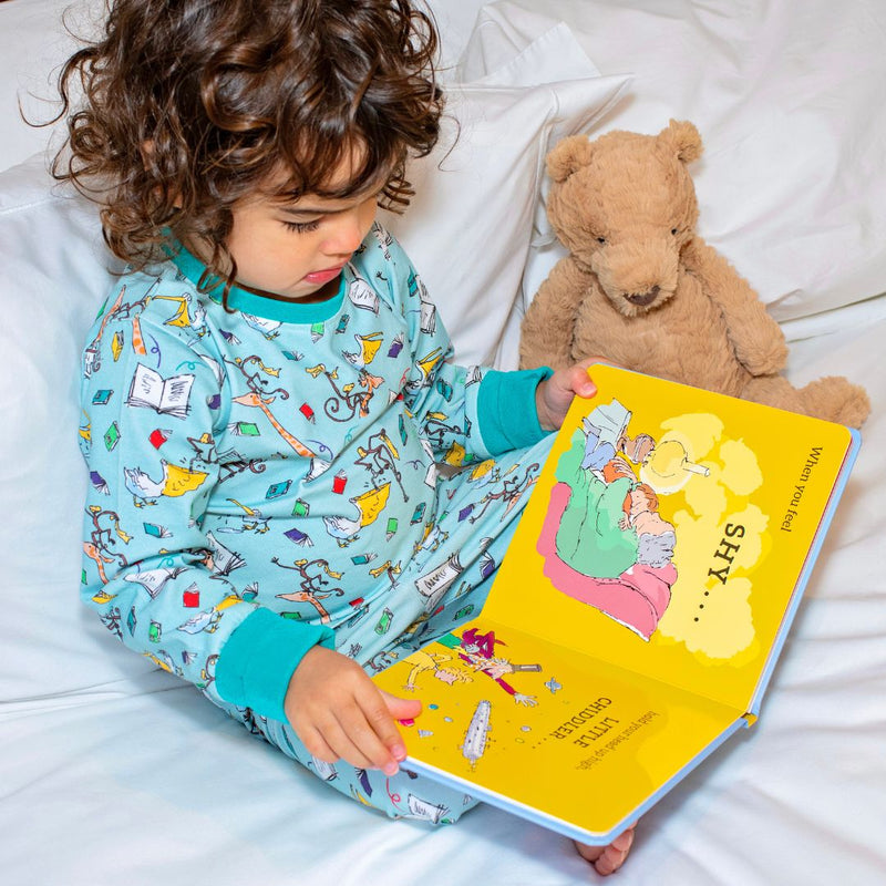 Image of a girl sitting in bed, reading a Roald Dahl book, wearing a pair of Ducky Zebra x Roald Dahl aqua pyjamas