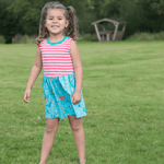 Young girl in a striped coral and blue dress standing in a grassy field