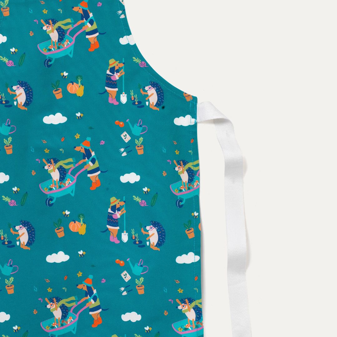 Close up of children's apron with a teal green background and fun repeat print of a gardening dog and hedgehog.