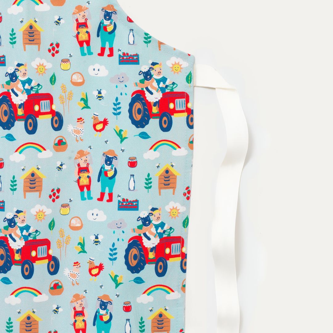 Close up of cotton children's apron with a fun farmyard print - with sheep and big driving their tractor and looking after the bees