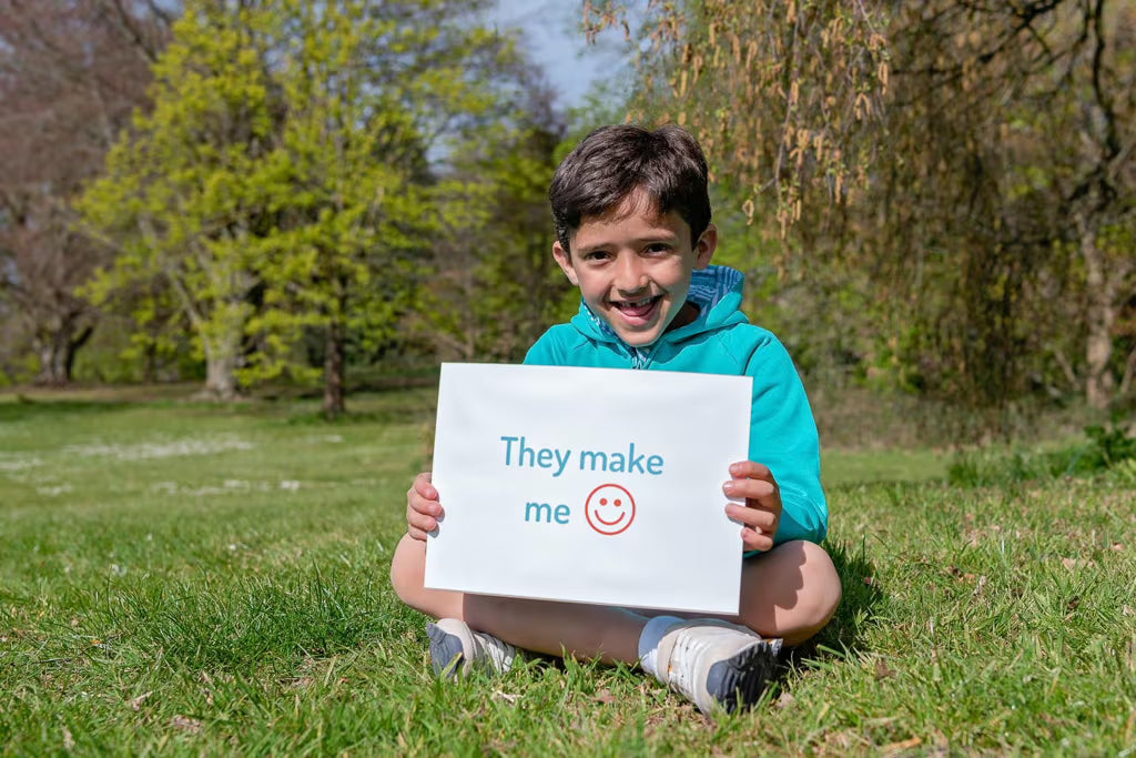 Child holding a sign with text and a smiley face in a park