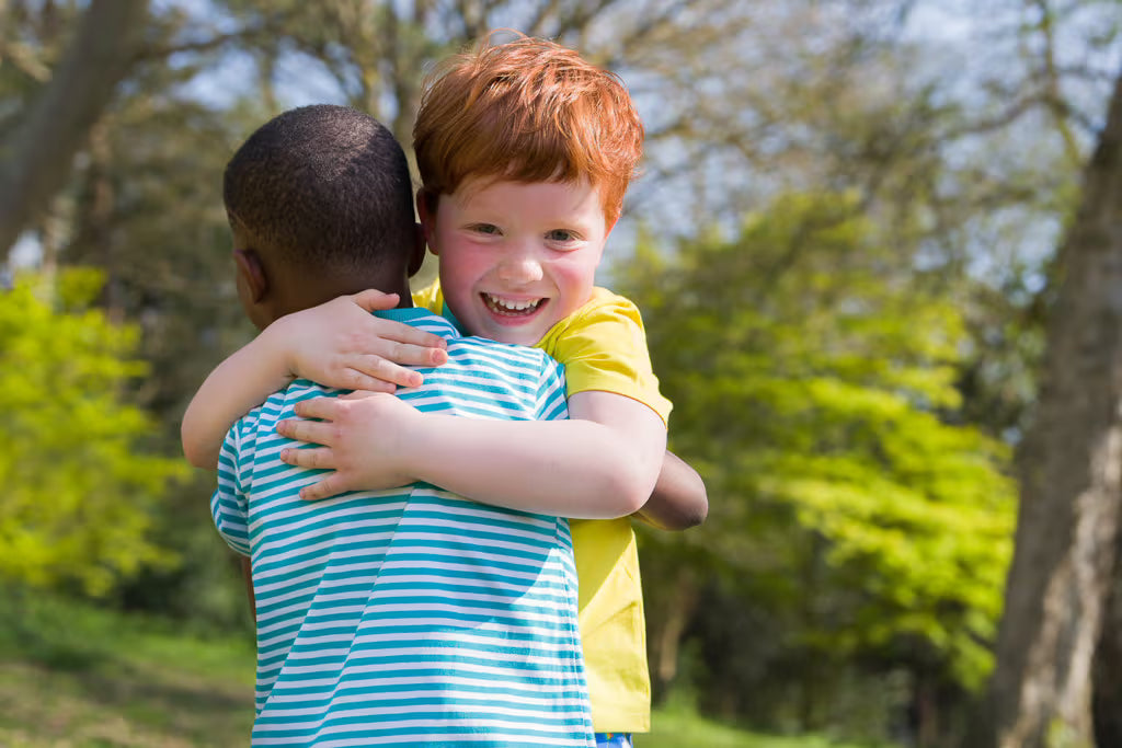 Two children hugging outdoors with trees in the background